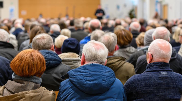 large group of residents attending town meeting. community members seated and listening to speaker in public hall. civic engagement and local discussion concept