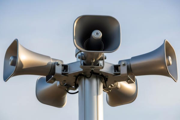 multiple gray horn loudspeakers on a pole against a clear blue sky. public announcement system for urgent messages and emergency alerts.
